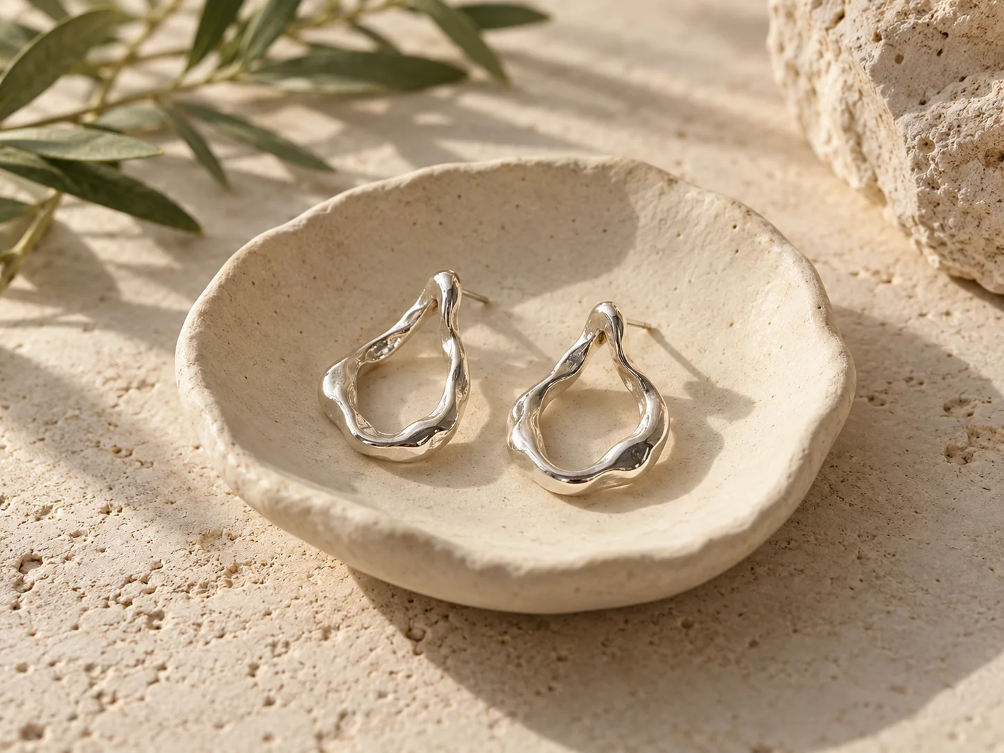Organic silver earrings resting on a handmade ceramic dish